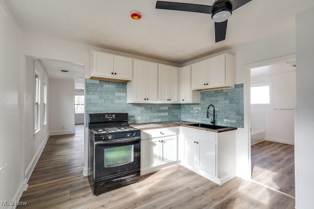 kitchen with gas stove, white cabinetry, sink, and light hardwood / wood-style floors