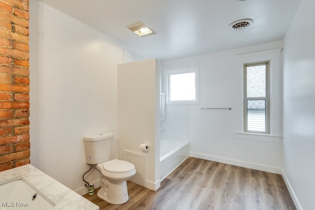 bathroom with a washtub, brick wall, toilet, vanity, and hardwood / wood-style flooring