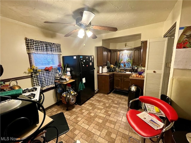 kitchen featuring black refrigerator, dark brown cabinets, a textured ceiling, ceiling fan, and sink