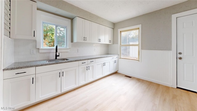 kitchen featuring sink, light stone counters, backsplash, light hardwood / wood-style floors, and white cabinets