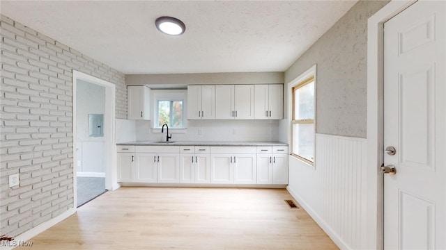 kitchen featuring light wood-type flooring, brick wall, a textured ceiling, sink, and white cabinetry