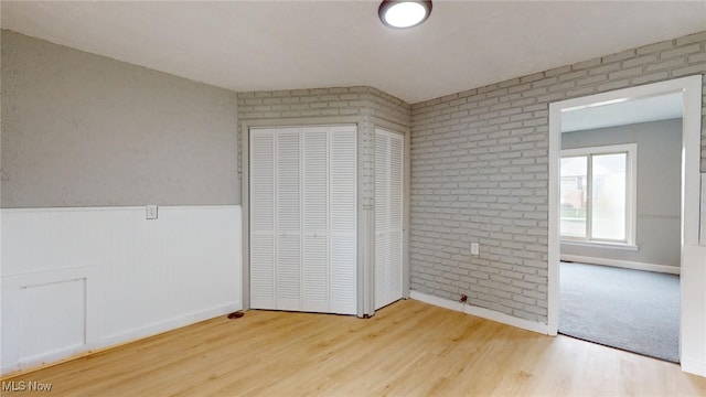 unfurnished bedroom with a closet, wood-type flooring, and brick wall