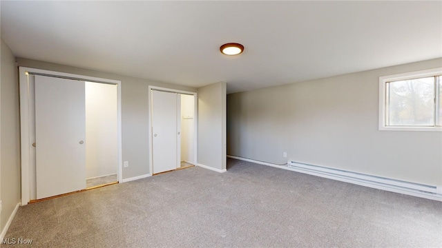 unfurnished bedroom with two closets, light colored carpet, and baseboard heating