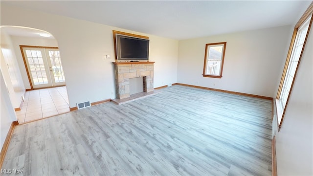 unfurnished living room featuring french doors, light hardwood / wood-style floors, a stone fireplace, and a healthy amount of sunlight