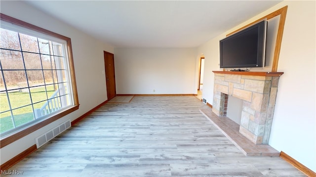 unfurnished living room featuring light hardwood / wood-style floors and a stone fireplace