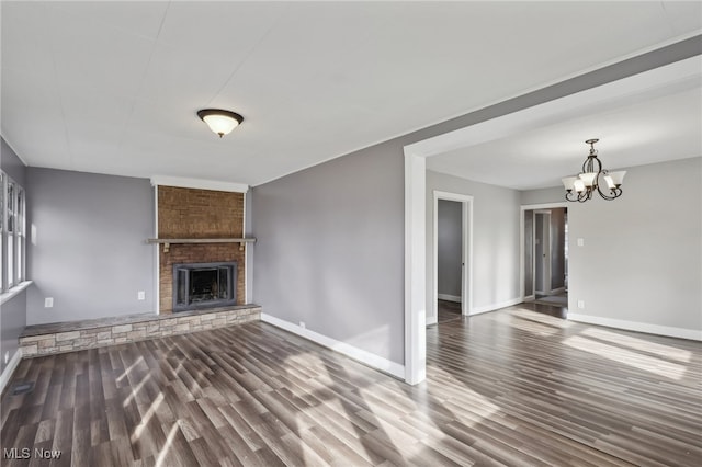 unfurnished living room with a brick fireplace, dark hardwood / wood-style flooring, and an inviting chandelier