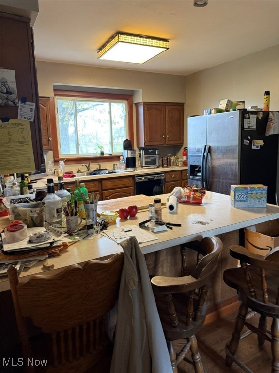 kitchen featuring sink, black dishwasher, dark hardwood / wood-style floors, stainless steel refrigerator with ice dispenser, and a breakfast bar area