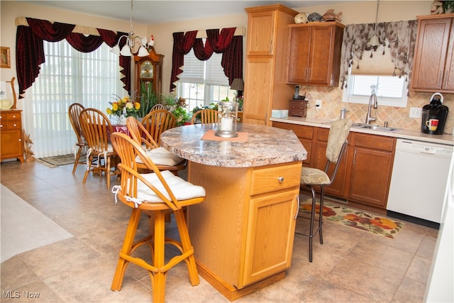 kitchen with white dishwasher, a kitchen breakfast bar, a kitchen island, and a healthy amount of sunlight