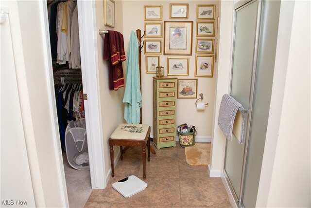 full bath with a spacious closet, a shower stall, and baseboards