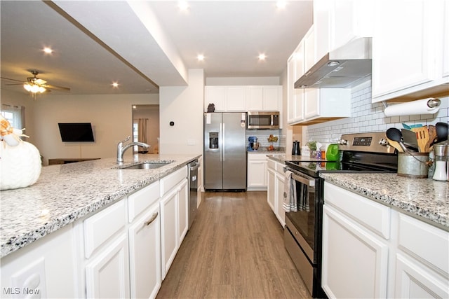 kitchen with wall chimney range hood, ceiling fan, light wood-type flooring, white cabinetry, and stainless steel appliances