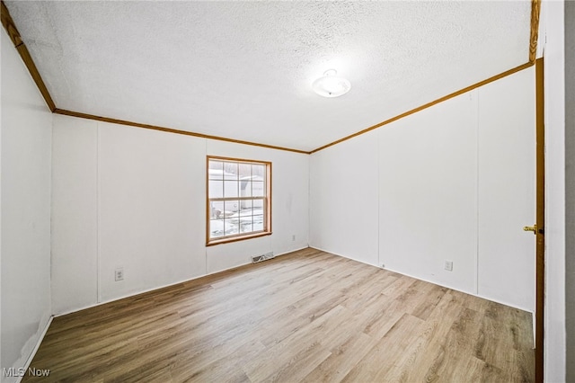 spare room featuring ornamental molding, light hardwood / wood-style floors, and a textured ceiling