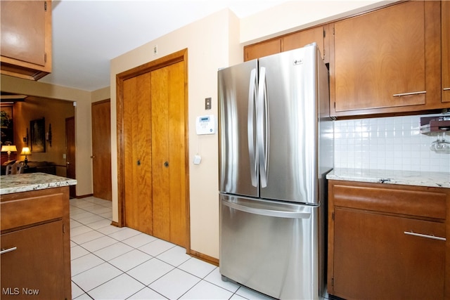 kitchen featuring backsplash, stainless steel refrigerator, light stone countertops, and light tile patterned flooring