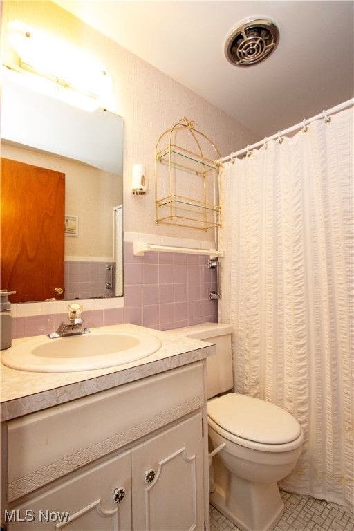 bathroom featuring tile patterned flooring, vanity, toilet, and tile walls