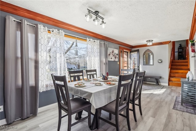 dining room with light hardwood / wood-style floors, a textured ceiling, and ornamental molding