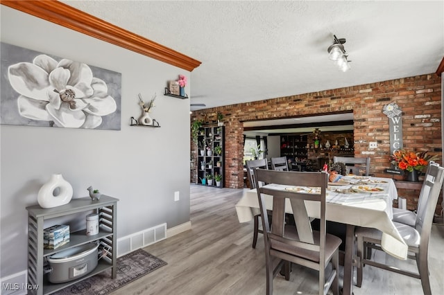 dining area featuring brick wall, a textured ceiling, and hardwood / wood-style flooring