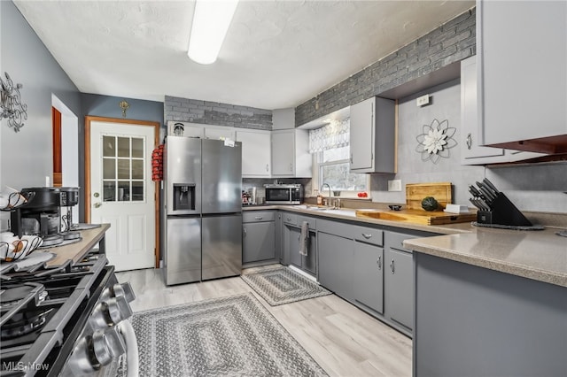 kitchen with gray cabinetry, sink, appliances with stainless steel finishes, and light hardwood / wood-style flooring