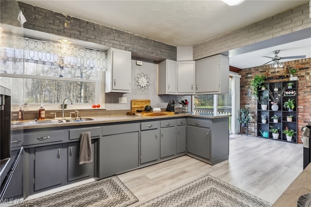 kitchen with a wealth of natural light, gray cabinets, sink, and brick wall