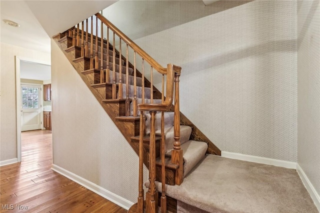 staircase with wallpapered walls, baseboards, and wood-type flooring