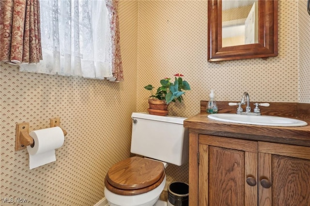 half bath featuring wallpapered walls, toilet, and vanity