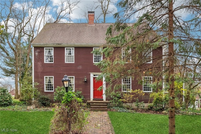 colonial inspired home with a chimney, a front lawn, and roof with shingles