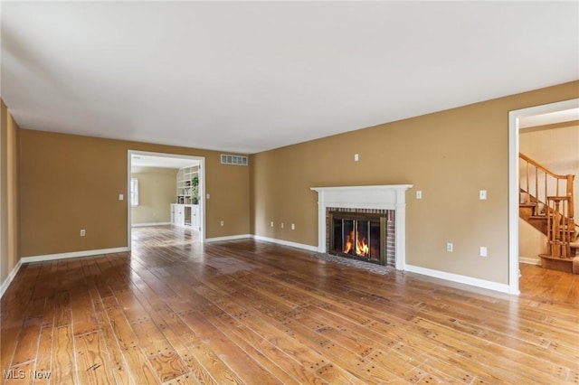 unfurnished living room with visible vents, hardwood / wood-style flooring, a fireplace, baseboards, and stairs