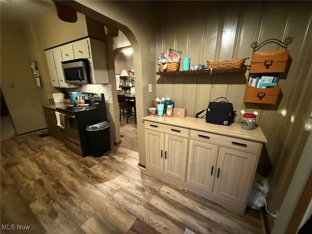 kitchen featuring black electric range, light wood-type flooring, and tasteful backsplash