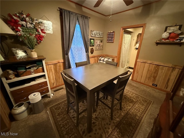 carpeted dining area with ceiling fan and wood walls