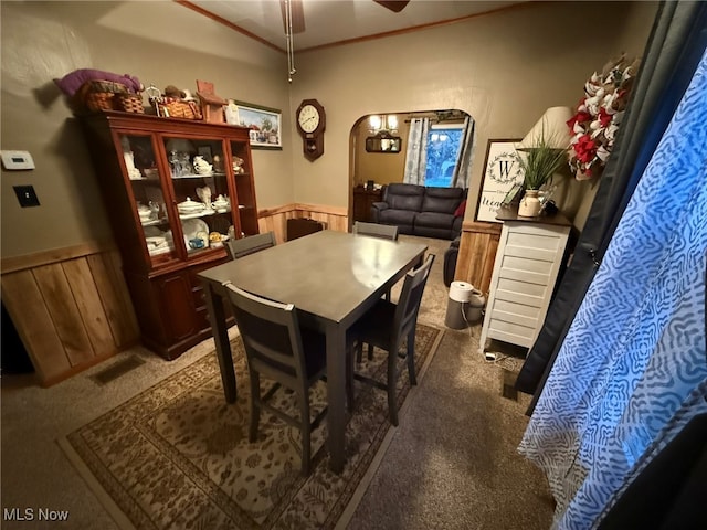 dining area with wood walls, ceiling fan, and dark carpet