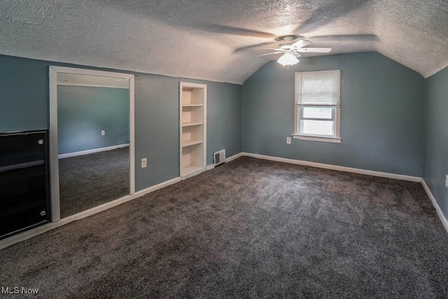 additional living space with dark carpet, a textured ceiling, vaulted ceiling, and ceiling fan