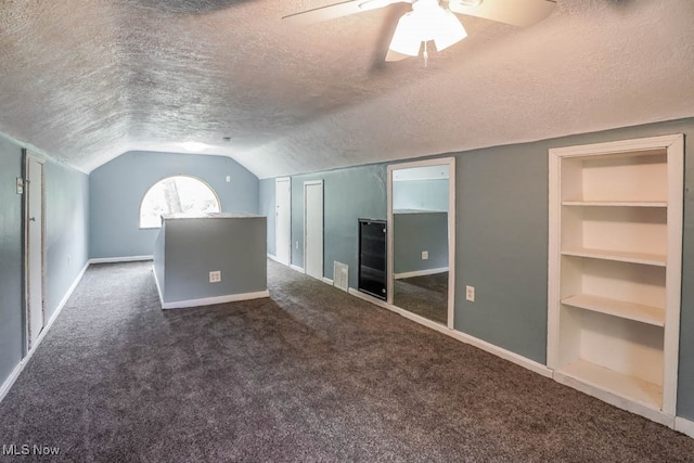 bonus room with built in shelves, a textured ceiling, vaulted ceiling, ceiling fan, and dark colored carpet