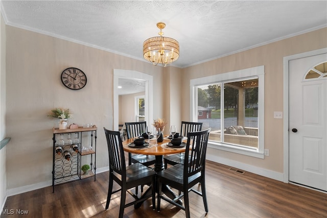 dining area with dark wood-type flooring, a chandelier, a textured ceiling, and ornamental molding