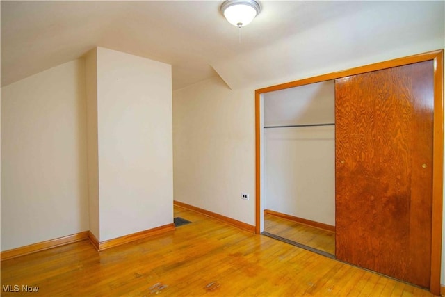 unfurnished bedroom featuring hardwood / wood-style flooring, vaulted ceiling, and a closet