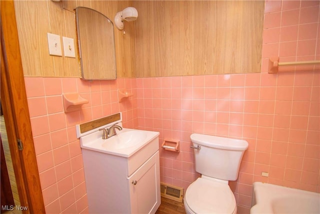 bathroom featuring vanity, a bath, toilet, and tile walls