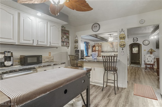 kitchen featuring dishwasher, a kitchen bar, light wood-type flooring, and white cabinetry