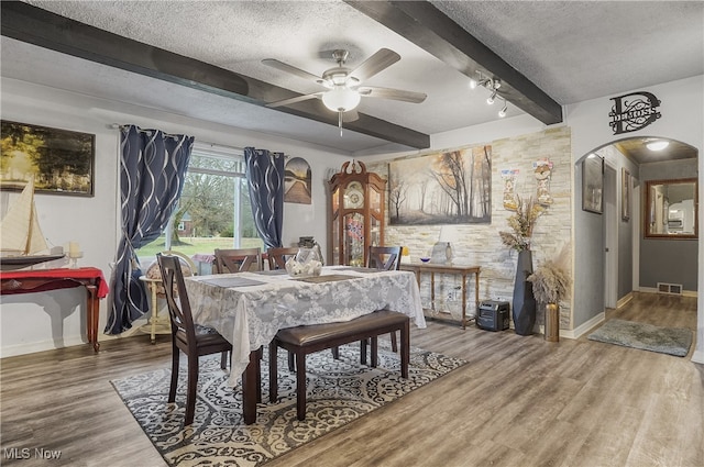 dining room with ceiling fan, beam ceiling, wood-type flooring, and a textured ceiling