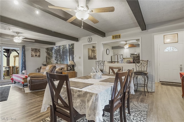 dining space featuring beam ceiling, light hardwood / wood-style floors, and a textured ceiling