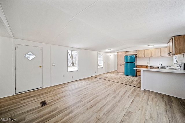 kitchen with vaulted ceiling, fridge, a textured ceiling, and light wood-type flooring