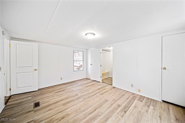 unfurnished bedroom featuring ensuite bathroom, a textured ceiling, and light wood-type flooring