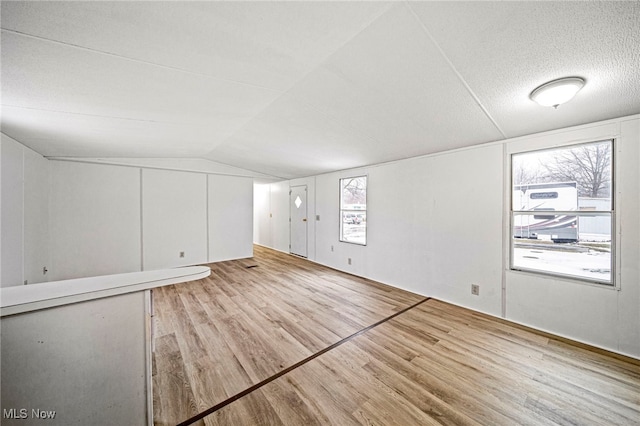 additional living space featuring lofted ceiling, a textured ceiling, and light hardwood / wood-style flooring