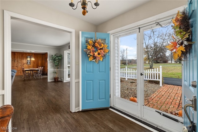 doorway to outside featuring wooden walls, ornamental molding, dark wood-type flooring, and an inviting chandelier