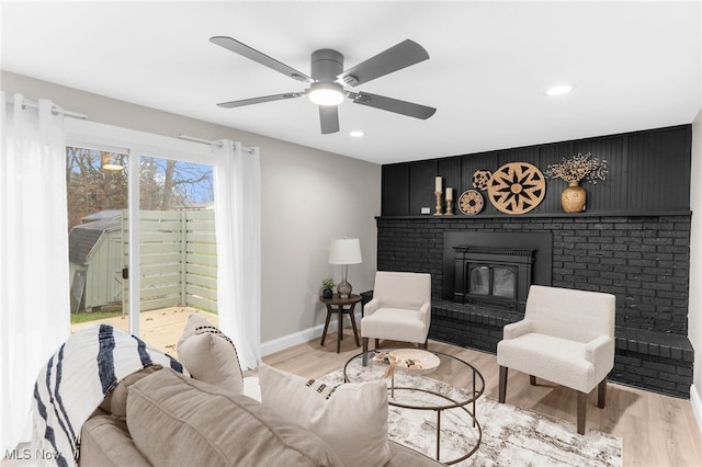 living room featuring a wood stove, ceiling fan, and light hardwood / wood-style floors