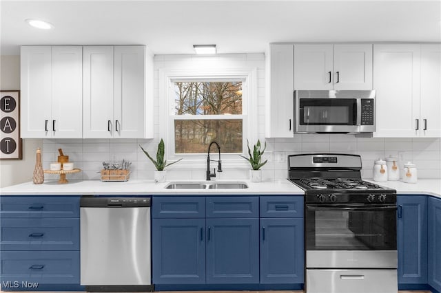 kitchen with decorative backsplash, appliances with stainless steel finishes, blue cabinets, sink, and white cabinetry