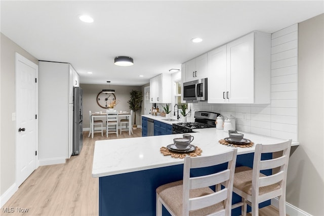 kitchen with backsplash, white cabinets, sink, light wood-type flooring, and stainless steel appliances