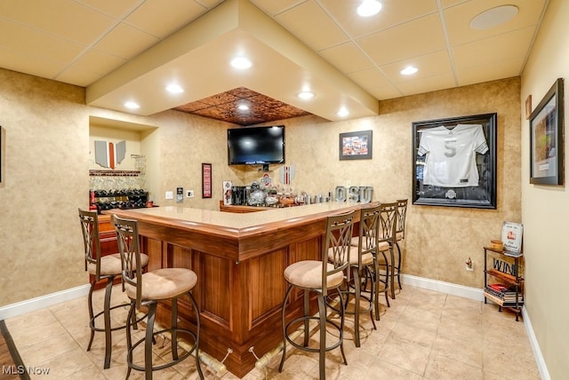 bar with a paneled ceiling and light tile patterned flooring