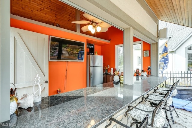 kitchen featuring ceiling fan, stainless steel fridge, wood ceiling, and dark stone counters