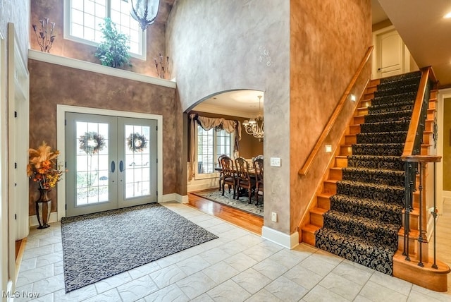 foyer with french doors, a towering ceiling, crown molding, a chandelier, and light hardwood / wood-style floors