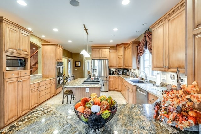 kitchen with light stone countertops, appliances with stainless steel finishes, a kitchen bar, sink, and hanging light fixtures