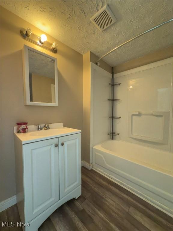 full bath featuring a textured ceiling, visible vents, wood finished floors, and bathing tub / shower combination