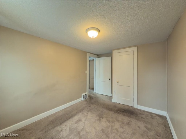 unfurnished bedroom featuring a textured ceiling, light colored carpet, visible vents, baseboards, and a closet