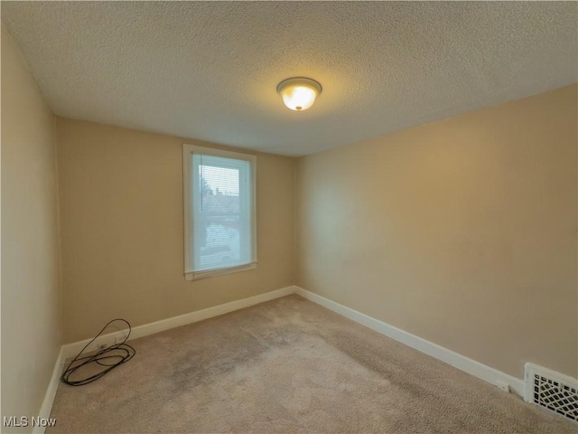 spare room featuring light colored carpet, visible vents, a textured ceiling, and baseboards